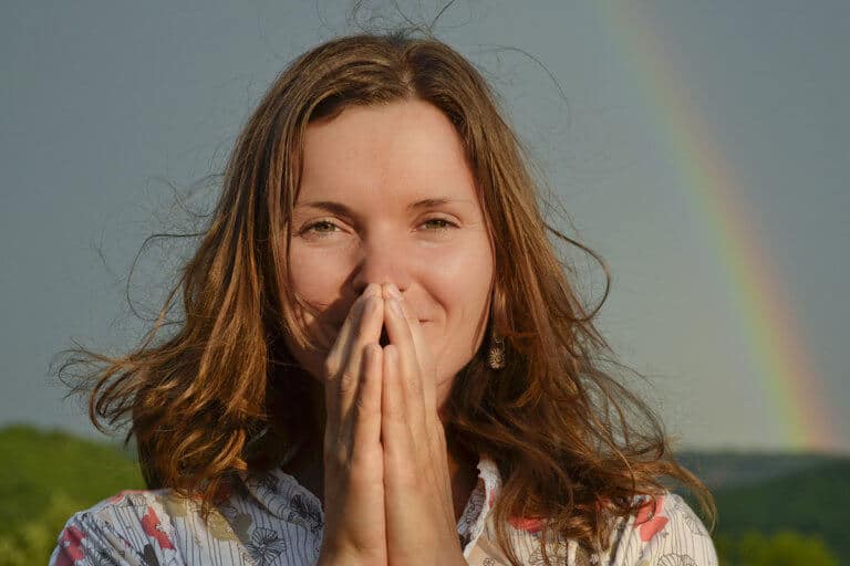 a woman stands in front of a rainbow thinking about faith trust and gratitude