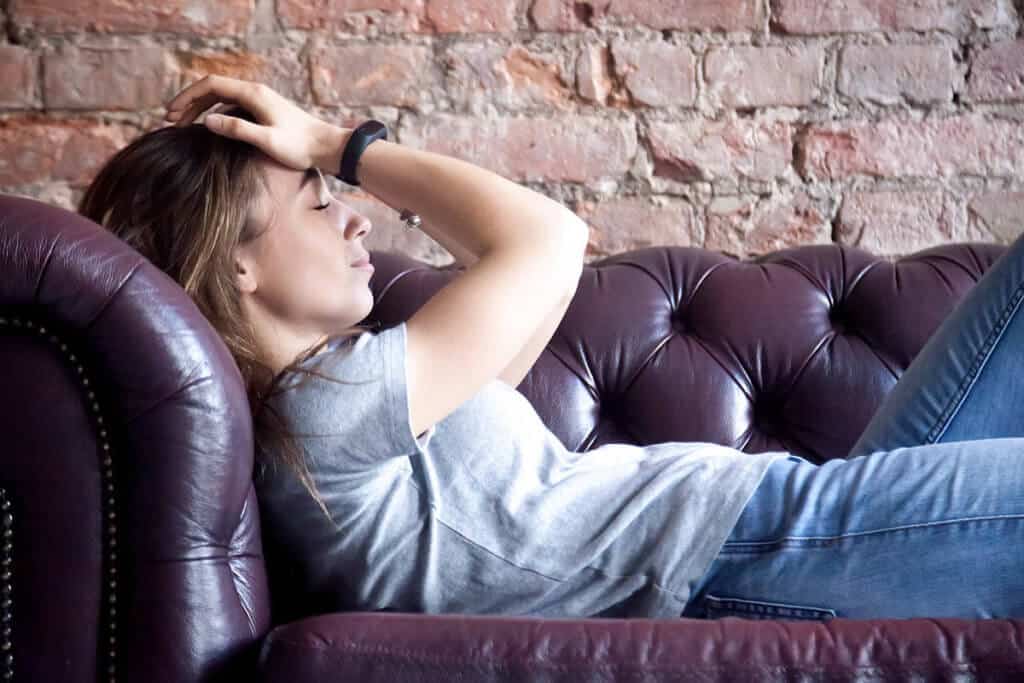 girl laying on couch with hands on head experiencing heroin withdrawal symptoms