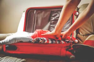 person packs open suitcase sitting on bed while looking up what to bring to rehab