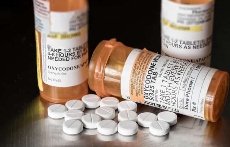 multiple prescription bottles with pills on the table show difference between opiate vs opioid