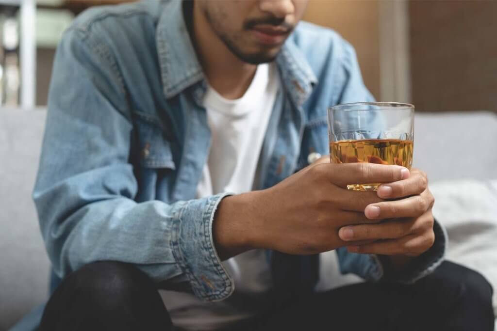 A man holds a drink as he asks himself, "Am I an alcoholic?"